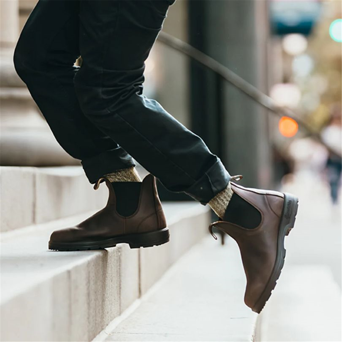A lifestyle shot of a person walking down a city street wearing rich brown Blundstone 2340 Classic Series Chelsea boots.