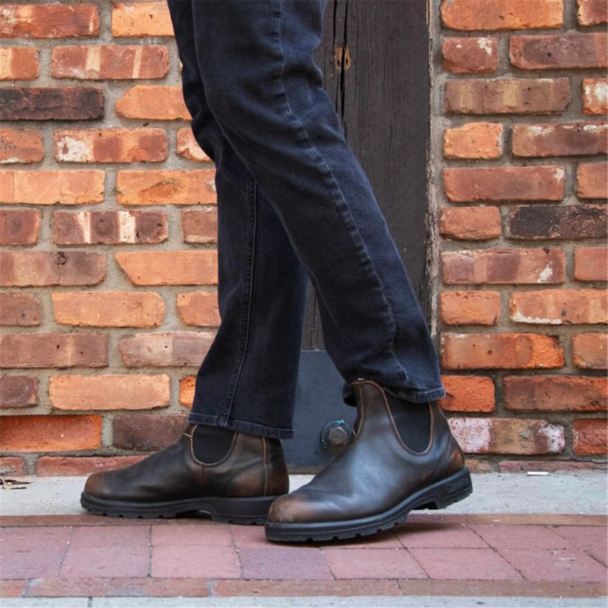 A person wearing denim jeans paired with vintage brown Blundstone 2440 Classic Series Chelsea boots.