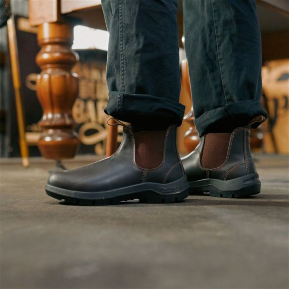 Low-angle shot of a person wearing dark brown leather Blundstone 710 Chelsea work boots with dark, cuffed trousers